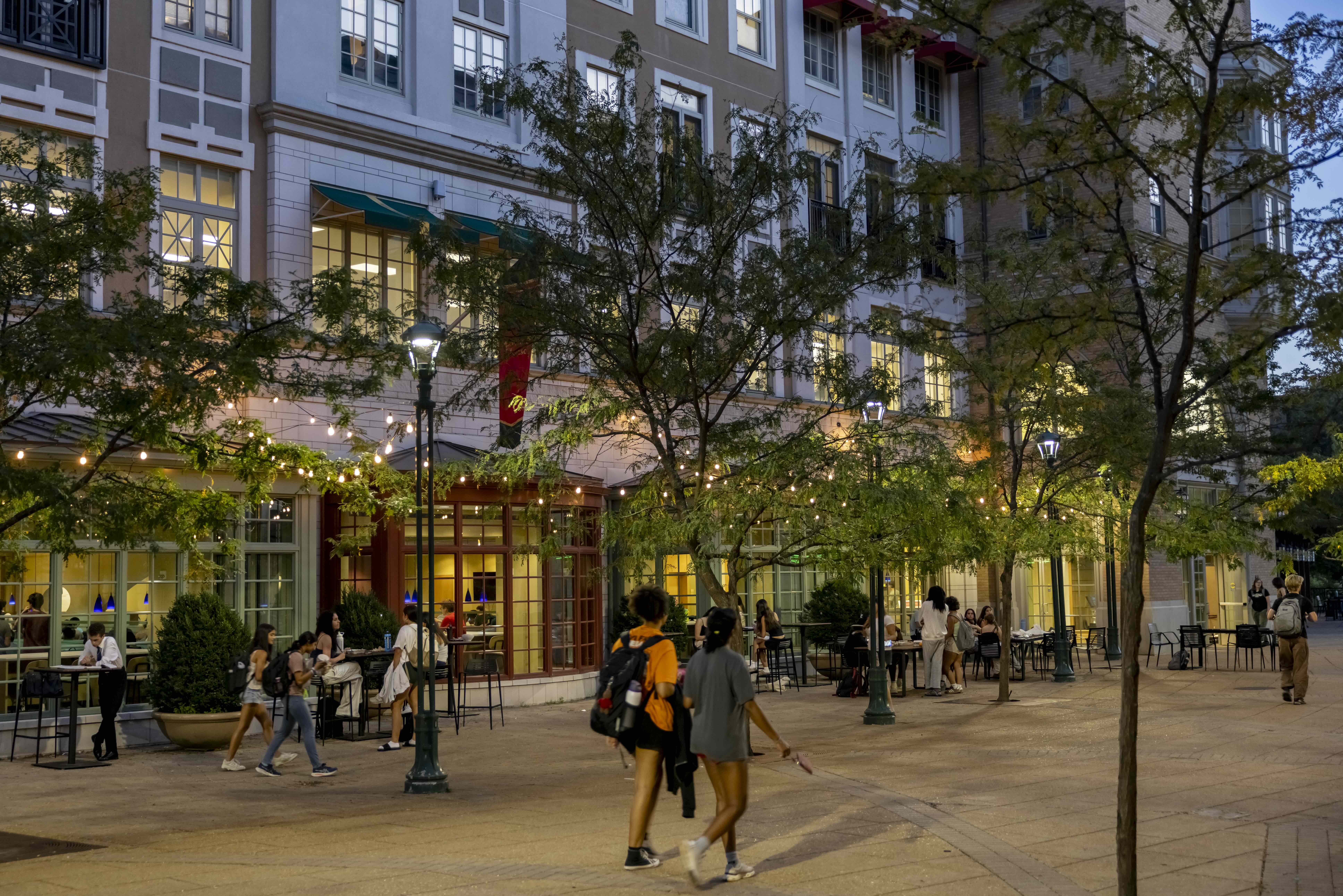 Young adults walk through an outdoor shopping area at dusk.